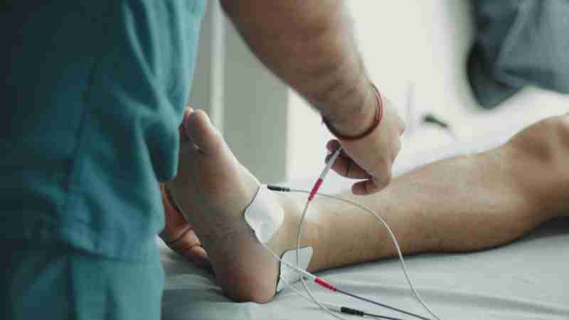 Close-up of a healthcare worker examining a patient's foot with medical equipment in a hospital setting., tags: die - pexel